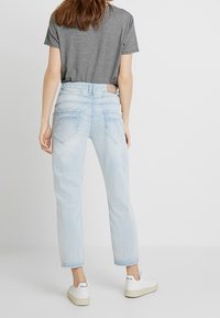 Světlé modré džíny s vysokým pasem a uvolněným střihem, mají pět kapes a lehce vybledlý vzhled. V kombinaci s černým a bílým vzorovaným topem a bílými teniskami.