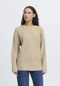 Maglione lavorato a maglia beige con scollatura rotonda, orlo a coste e dettagli testurizzati nei pannelli laterali. Maniche lunghe e vestibilità standard. Abbinato a jeans blu.