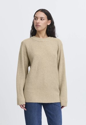 Beiger Strickpullover mit rundem Ausschnitt, geripptem Saum und seitlichen Texturdetails. Lange Ärmel und normale Passform. Kombiniert mit blauer Jeans.