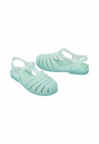 Miętowe plastikowe sandały z poziomymi i pionowymi wycięciami, regulowanym paskiem i płaską podeszwą. Lekka i elastyczna konstrukcja.