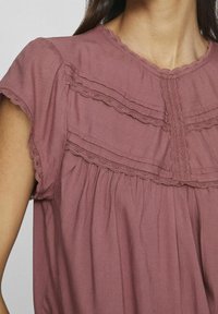 Blusa mauve arricciata con maniche corte, caratterizzata da un bordo in pizzo e dettagli arricciati al colletto e al torso per un effetto texture aggiuntivo.