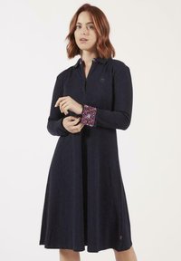 Robe navy avec col, fermeture éclair à l'avant et manches longues. Tissu à motif floral sur les poignets. Texture douce, forme évasée, longueur mi-mollet.