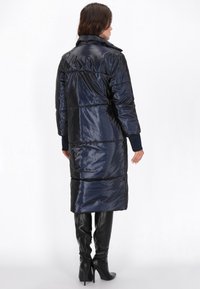 Lang navy blue puffer coat med høj krave, tekstureret finish og sidelommer, parret med højre støvler i sort med hæl.