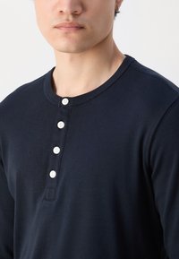 Marineblå langermet henley-skjorte med rund hals og fem hvite knapper foran. Laget av glatt, myk stoff.