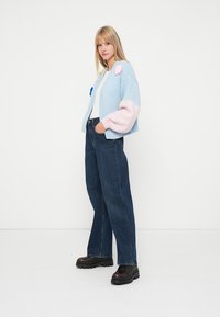 Ανοιχτό μπλε πουλόβερ με ροζ μανίκια και λουλουδάτα απλικέ, συνδυασμένο με ψηλόμεσα σκούρα τζιν και μαύρα παπούτσια με χοντρή σόλα.