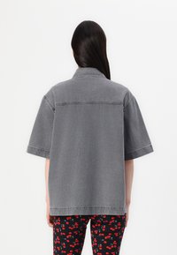 Grå denimjakke med løs passform, korte ermer og en søm over ryggen. Kombinert med leggings med et rødt kirsebærmønster.