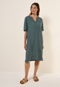Teal kortärmad klänning med V-ringning, något lös passform, sidospagater och texturerad stof. Matchad med bruna sandaler med spänne.