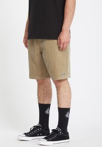 Beige kordfløjlshorts med sidelommer og et lille logo, parret med sorte strømper og sorte lærredssneakers.