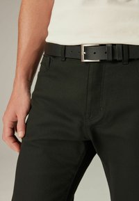 Zwarte denim broek met een subtiele textuur, voorzien van een voorzak en een zilveren metalen gesp riem met een gestructureerde afwerking.