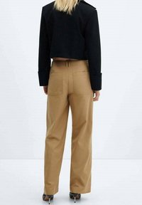 Zwarte cropped blazer met schouderaccenten, gecombineerd met beige wijde broek met achterzakken. Smooth stof en strakke lijnen.