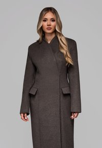 Lang brun uldfrakke med et elegant design, indpakningsstil og sidelommer. Har en høj krave og lige snit for et skræddersyet udseende.