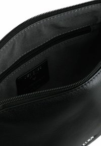 Schwarze Lederhülle mit glatter Oberfläche, Reißverschluss und grauem Stofffutter. Enthält ein Etikett mit der Aufschrift "Designed with ❤️ in Germany."