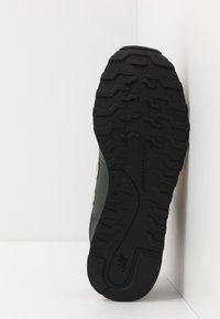 Svart gummi sula med texturerat mönster, kompletterad av en grön ovandel med vita och orange detaljer.