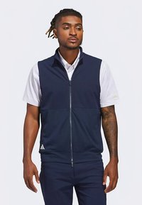 Mornarsko plavi prsluk na patent s okovratnikom, izrađen od laganog materijala. Ima dva bočna džepa i prepoznatljivi logo s tri pruge na rubu.