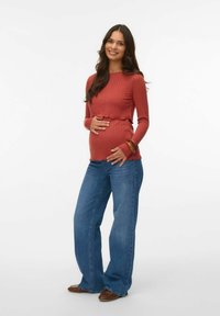 Mörkröd ribbade långärmade topp med volangkant, i kombination med ljusblå utsvängda jeans. Modellen håller om magen, med träarmband på handleden.