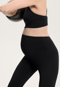Črn športni top s tankimi naramnicami in leggice iz raztegljivega, gladkega materiala. Leggice so zasnovane tako, da podpirajo trebuh.