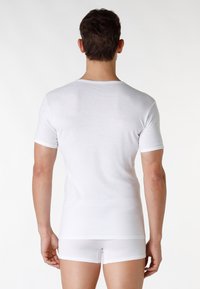 T-shirt bianco a maniche corte realizzato in tessuto morbido, con scollatura rotonda e design aderente, indossato con pantaloni corti bianchi. Texture liscia.