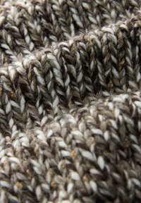 Close-up of thick knitted fabric with interwoven brown, beige, and white yarn strands creating a textured, cozy pattern.