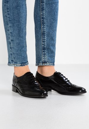 Sorte laklædersko i oxfordstil med snøredesign, indviklede perforeringer og lav hæl. Bruges med korte blå denimjeans.