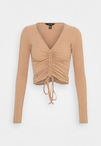 Långärmad, kort topp i en ljusbeige ribbad tyg med djup V-ringning, rynkad frontdetalj och justerbar snörning i fållen.