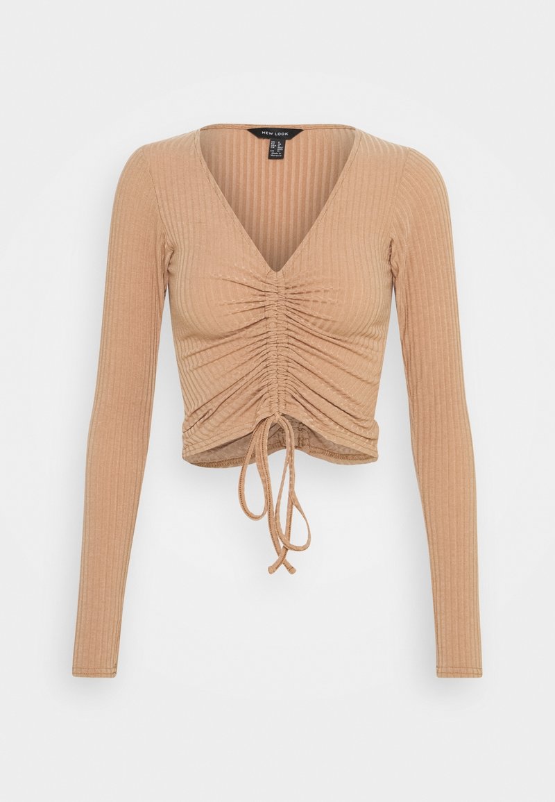 Långärmad, kort topp i en ljusbeige ribbad tyg med djup V-ringning, rynkad frontdetalj och justerbar snörning i fållen.