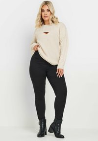 Maglione beige a maglia con dettaglio a taglio, abbinato a jeans skinny neri e stivali neri alla caviglia. Texture morbida e vestibilità rilassata.