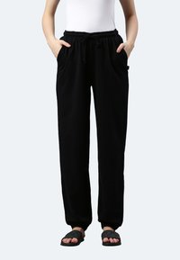 Schwarze Jogginghosen aus weichem Stoff, mit einem elastischen Bund und Kordelzug, Seitentaschen und schmal zulaufenden Bündchen.