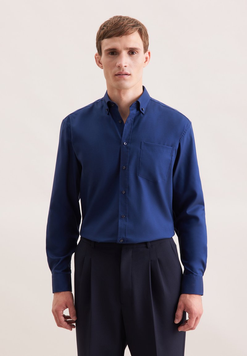 Marineblauwe shirt met lange mouwen van een gladde stof, voorzien van een button-down kraag en een borstzak, gecombineerd met donkere broeken.