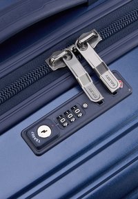 Valigia rigida blu navy con doppie cerniere argento e lucchetto a combinazione approvato dalla TSA. Presenta una superficie testurizzata e il logo del marchio.