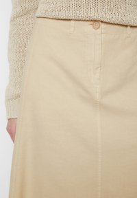 Beige Baumwollrock mit geradem Schnitt, ausgestattet mit einem Knopfverschluss und sichtbaren Nähten. Die Textur wirkt glatt und strapazierfähig.