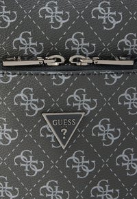 Mustast kunstnahast rahakott, millel on reljeefne logomuster, hõbedased aksessuaarid ning esiküljel kolmnurkne embleem, millel on kiri "GUESS USA".