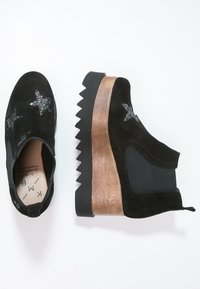 Botines de ante negro con adornos de estrellas plateadas, tacón de cuña de madera gruesa y suela de goma texturizada negra.