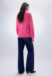 Csíkos rózsaszín hosszú ujjú felső, sötétkék, széles szárú farmerral, oldalsó díszítéssel. Sima textúra, laza szabás.