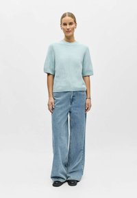 Pull en tricot bleu clair texturé avec des manches courtes bouffantes, assorti à un jean en denim léger à jambes larges et des chaussures noires.