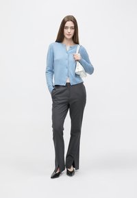 Light blue knitted cardigan, gray tailored trousers with slits at ankles, black pointed shoes, and a small white handbag. Simple, modern design.