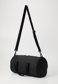 Zwarte duffelbag van duurzame stof, met een cilindervorm, twee stevige handvatten en een verstelbare schouderband met metalen hardware.