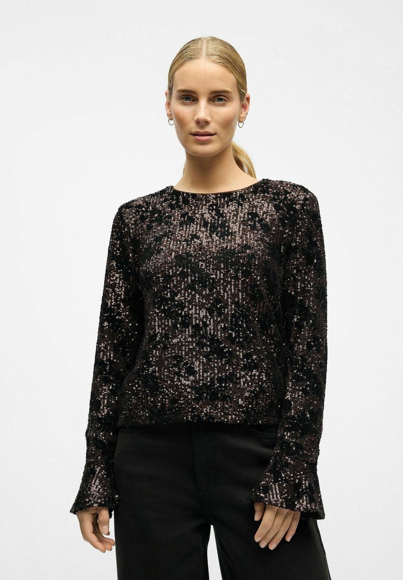 Black sequined sweater with long sleeves, flared cuffs, and textured fabric featuring a patterned overlay. Paired with black pants.