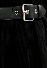 Tessuto di velluto a coste nero con righe verticali; presenta una cintura in pelle nera spessa con una fibbia in metallo argentato e occhielli.
