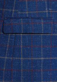 Niebieska tkanina w kratę o teksturowanym splocie, z klapą kieszeni i kontrastującymi czerwonymi i białymi liniami w wzór kratki.