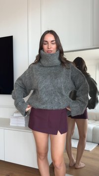 Übergroßer grauer Strickpullover mit einem hohen, umgeschlagenen Kragen und gerippten Bündchen. Dazu ein dunkelroter Minirock. Minimalistischer Hintergrund.