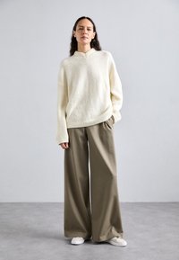 Cream sweater with a textured finish and wide sleeves, paired with high-waisted, wide-leg olive green trousers and white sneakers.