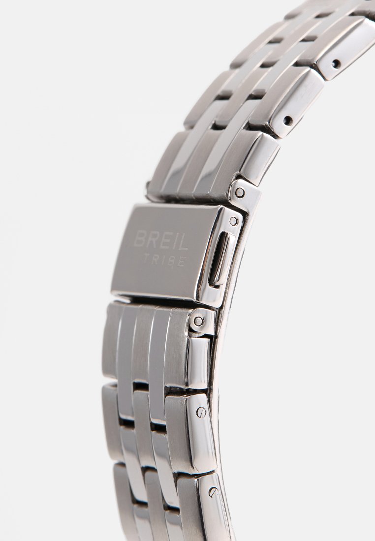 Reloj de pulsera de metal plateado con un diseño de brazalete vinculado. Presenta una superficie pulida y grabado "BREIL TRIBE" en el cierre.