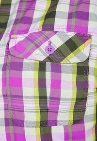 Košile s krátkým rukávem v několikatónovém kostkovaném vzoru v purpurové, zelené a žluté barvě, s kapsou na prsou a purpurovým knoflíkem.