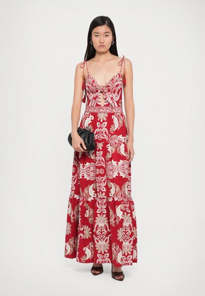 Red maxi dress with intricate white floral patterns, spaghetti straps, a keyhole detail, and ruffled hem; paired with a black clutch.