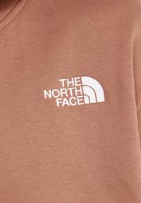 Sudadera marrón hecha de una mezcla de algodón. Presenta un logo bordado blanco con un diseño semicírculo. Textura suave y lisa.