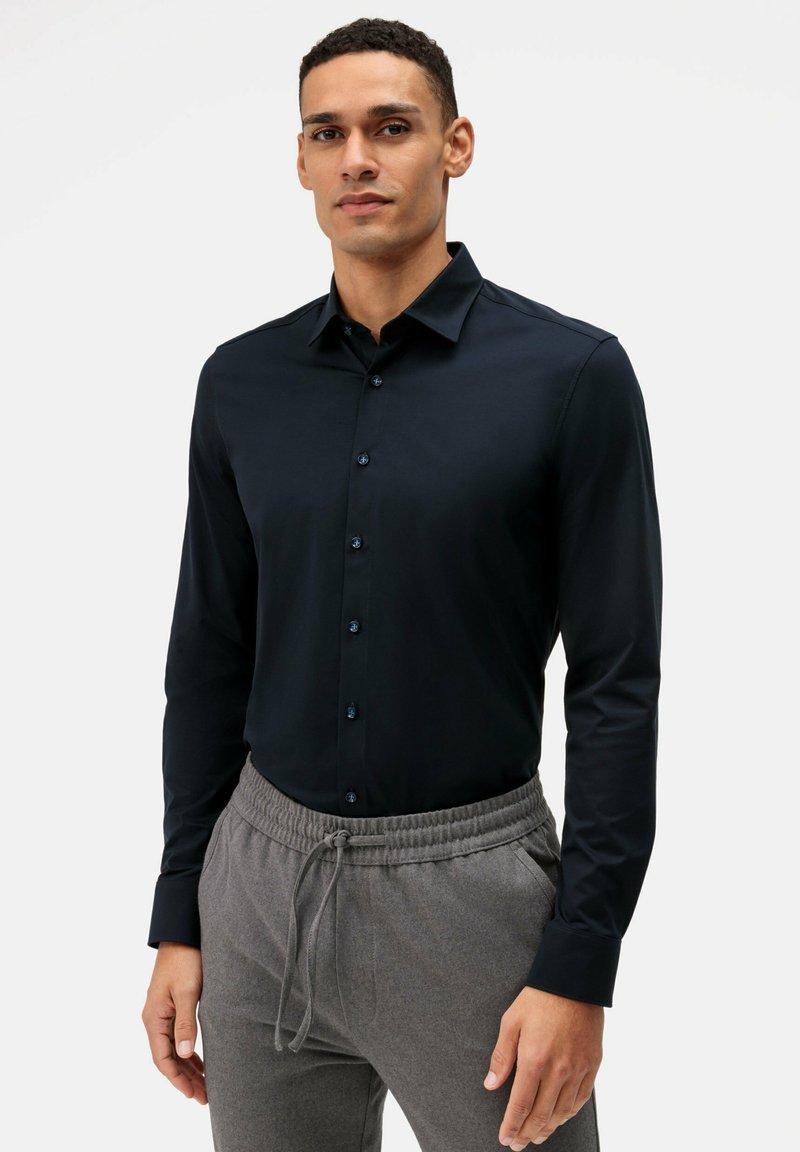 Camicia a maniche lunghe blu navy realizzata in tessuto morbido, con colletto tradizionale e chiusura frontale con bottoni, abbinata a pantaloni grigi con cordino.
