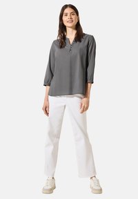 Blusa grigia a maniche lunghe con scollo a V e dettagli con bottoni. Abbinata a jeans bianchi a gamba dritta e sneakers chiari. Design pulito.
