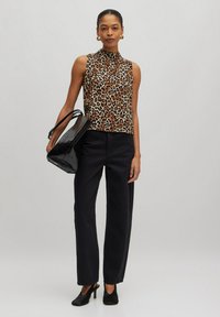 Ärmelloses Oberteil mit Leopardenmuster in Braun und Schwarz, kombiniert mit hoch-taillierten schwarzen Hosen und einer schwarzen, glanzvollen Tragetasche. Schwarze Absatzschuhe runden das Outfit ab.