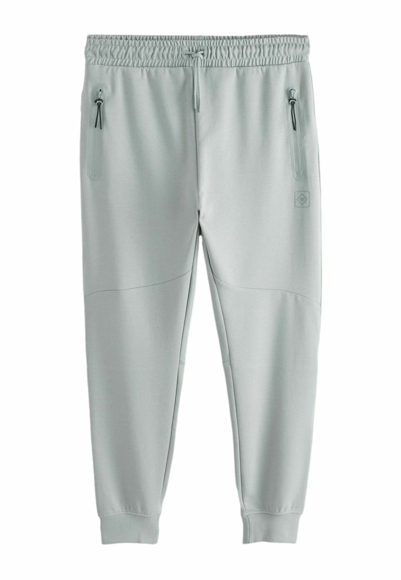 Pantaloni de trening gri deschis, cu un brâu elastic, două buzunare laterale cu fermoar și panouri din țesătură texturată pe laturi.