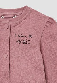 Różowy sweter o teksturowanej strukturze z okrągłym dekoltem, zapięciem na guziki oraz haftowanym napisem "wierzę W MAGI" z przodu.